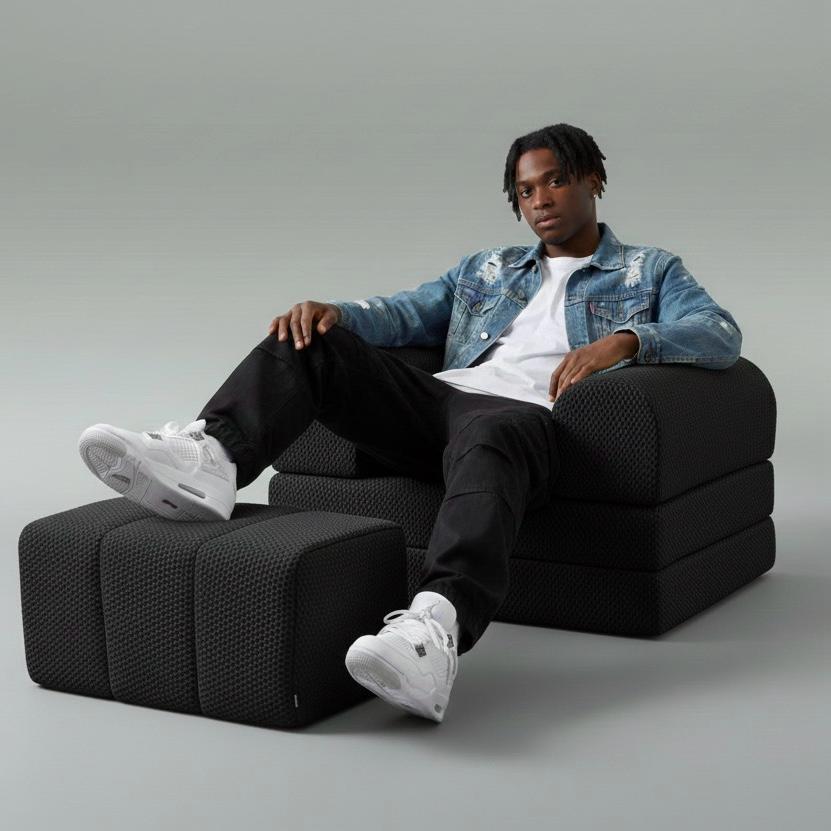 Person sitting on a Bro Single sofa resting his legs on a Black Ottoman  with  gray background